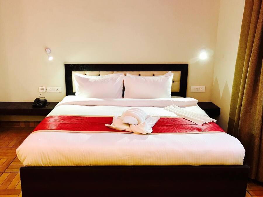 A neatly made bed with white linens and a red accent, a bedside phone, and a nightstand with a lamp.