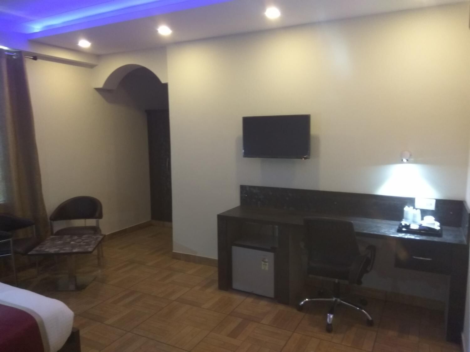 Una habitación de hotel con cama, escritorio con silla, televisor y refrigerador pequeño.