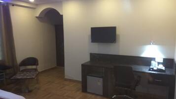 Una habitación de hotel con cama, escritorio con silla, televisor y refrigerador pequeño.