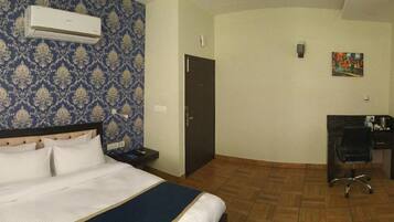 Una habitación de hotel con cama, escritorio, silla, aire acondicionado y puerta.