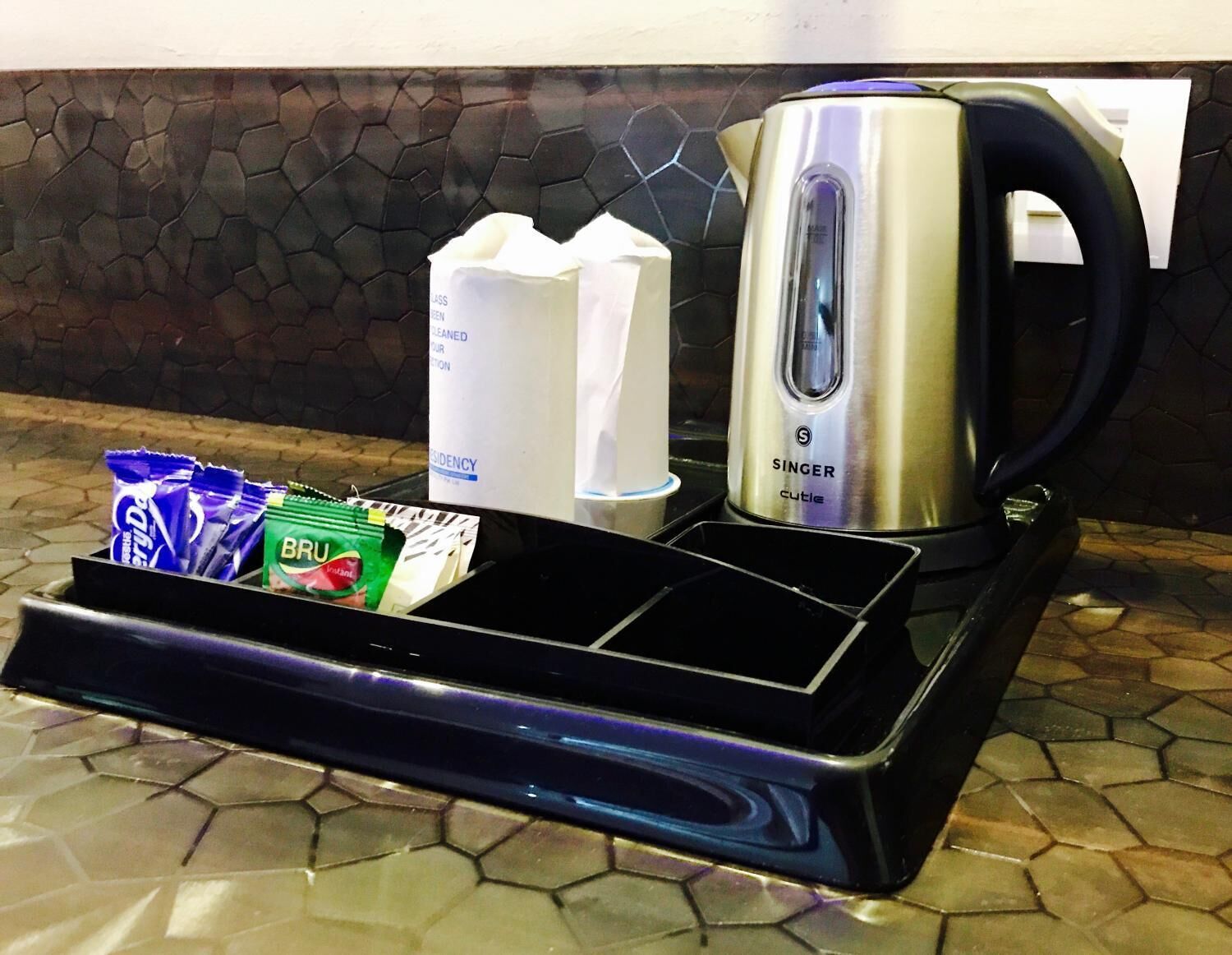 Een keukenhoek met een waterkoker, een koffiezetapparaat en een dienblad met lekkernijen en een fles water.