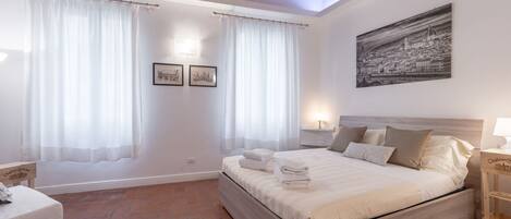 A bedroom with a bed, curtains, a painting, and a small bedside table.