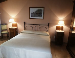 Una cama bien hecha con cabecera, dos mesitas de noche con lámparas, una silla y un cuadro en la pared.
