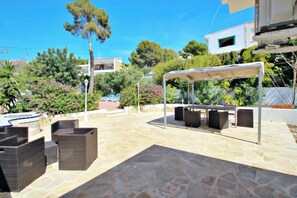 Un espace extérieur aménagé en terrasse, avec un sol en pierre, des meubles en osier et un coin salon ombragé.