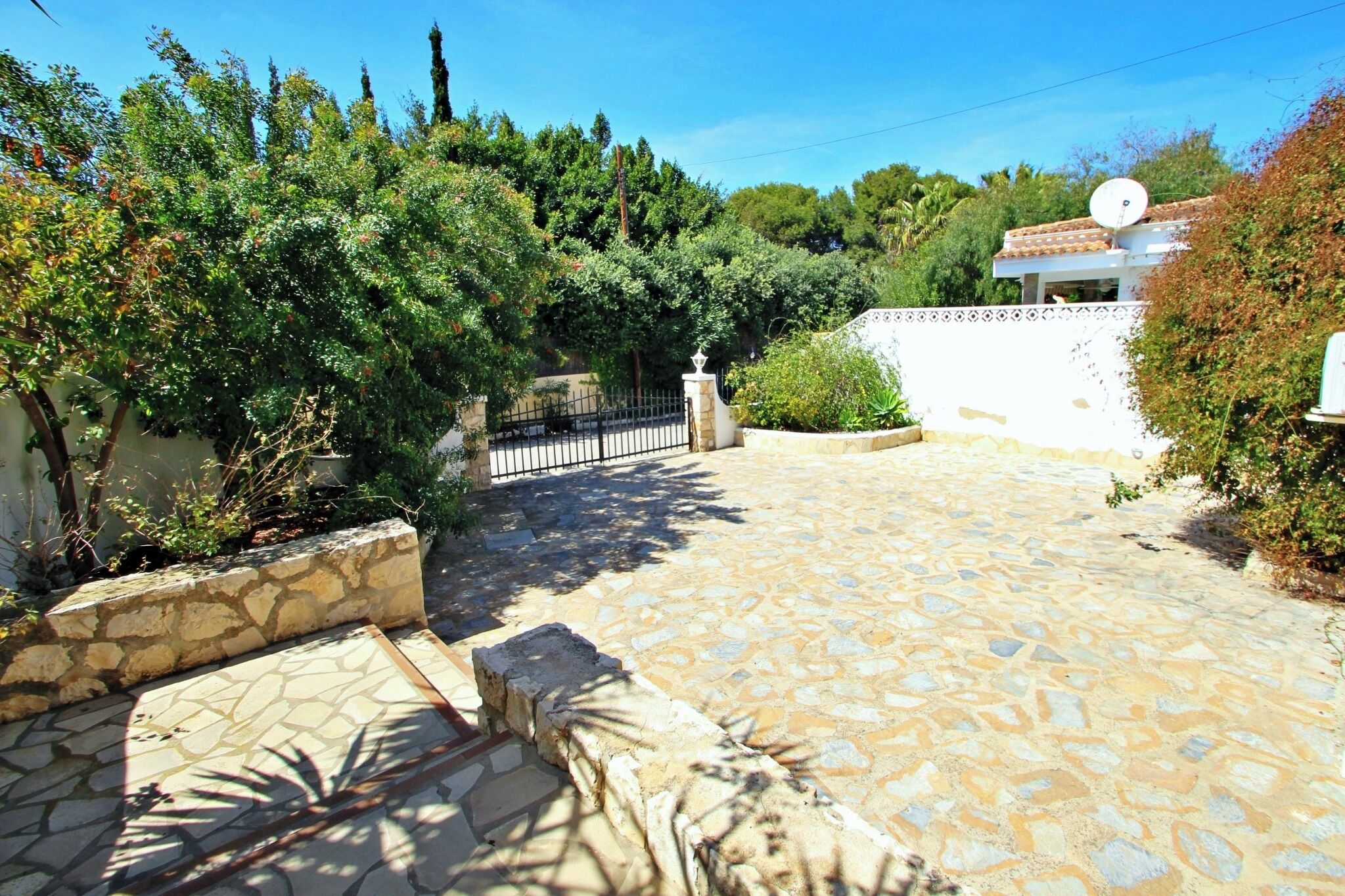 A stone-paved courtyard with a white wall and a gate.