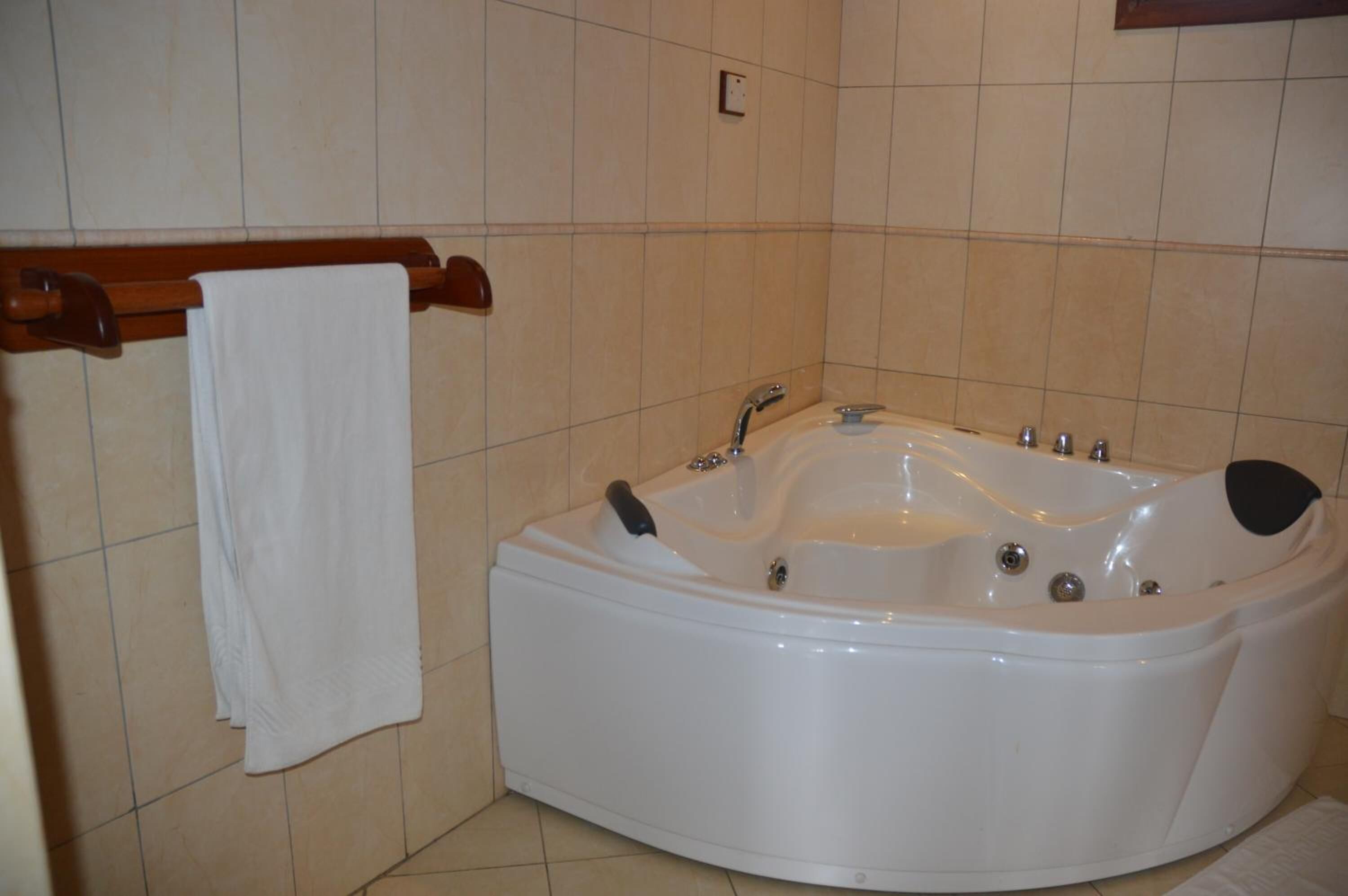 A bathroom with a white bathtub, a wooden towel rack, and beige tiled walls.