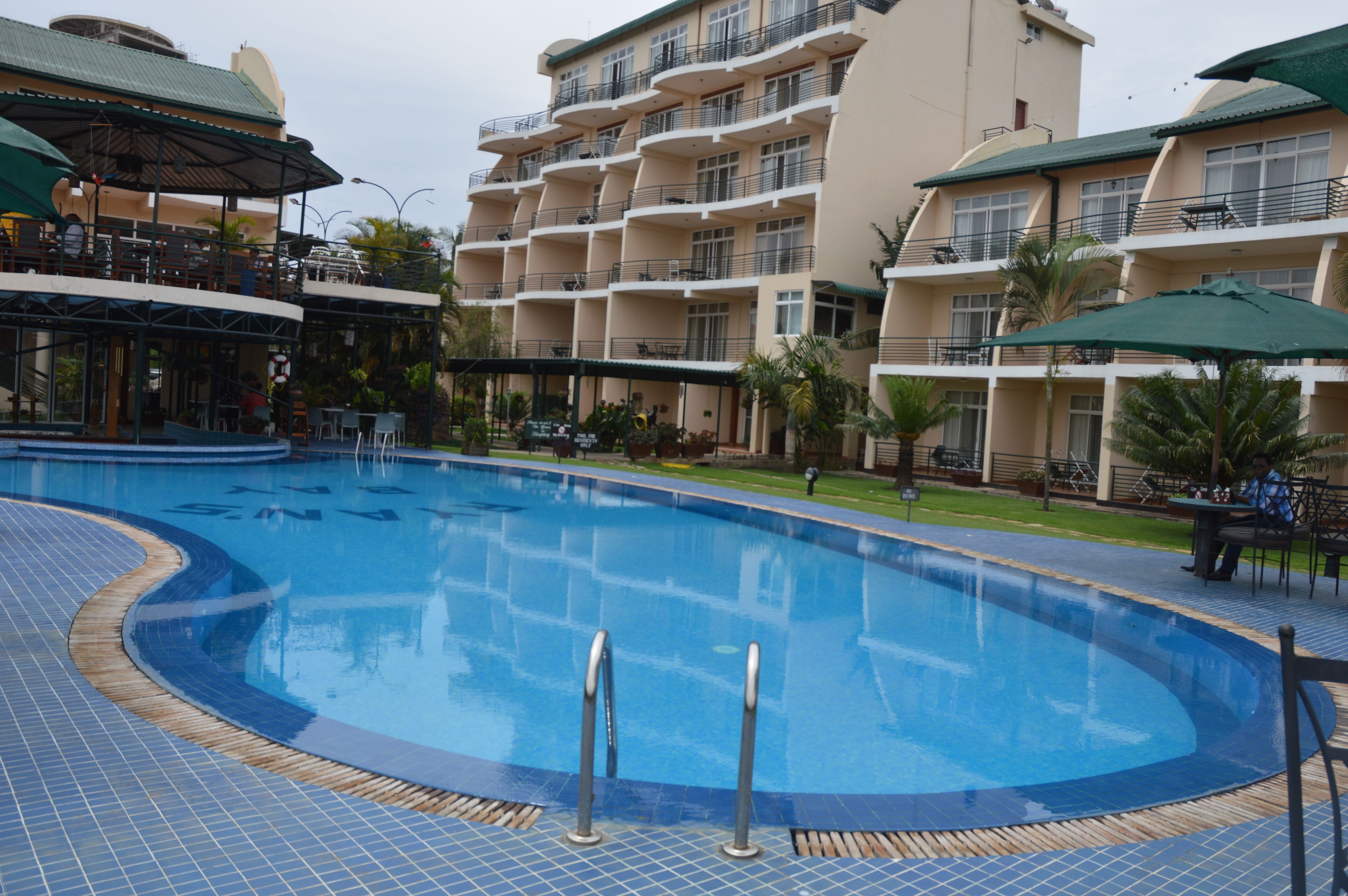 A swimming pool surrounded by a multi-story building with balconies, outdoor seating, and palm trees.