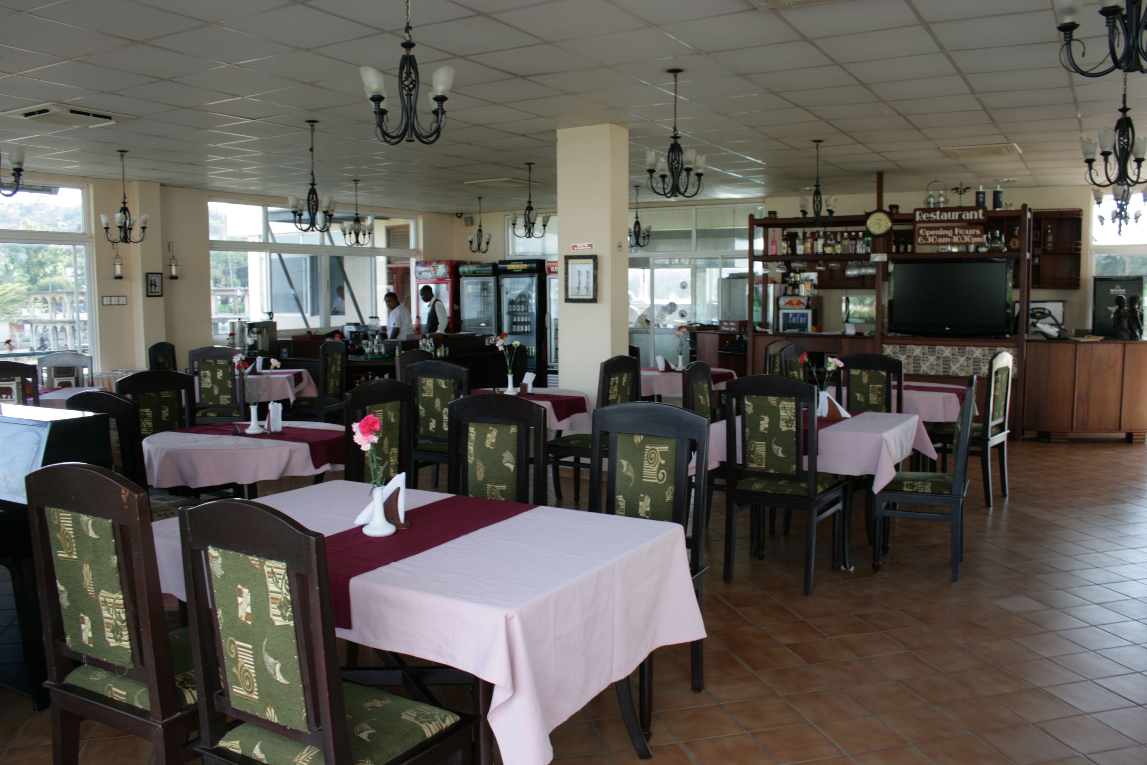A restaurant with multiple tables and chairs, a bar area, and a television screen.