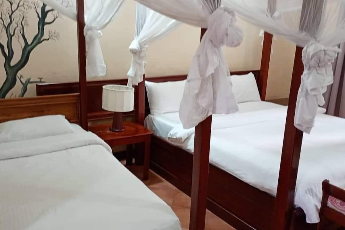 Ein Hotelzimmer mit zwei Betten, einem Nachttisch, einer Lampe und einem Wandgemälde eines Baumes.