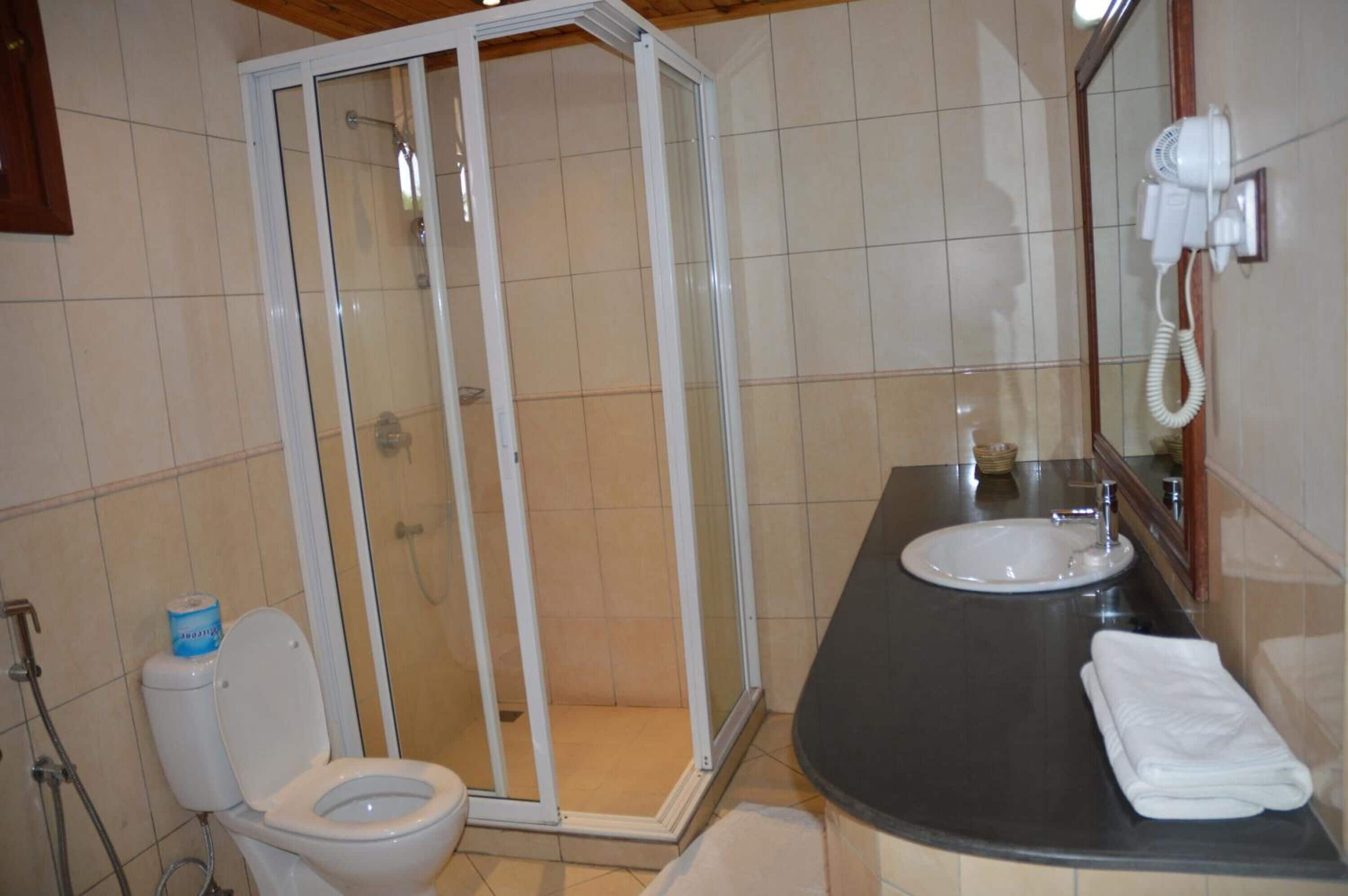 A bathroom with a shower enclosure, a toilet, a sink, and a hairdryer mounted on the wall.