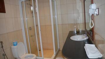 A bathroom with a shower enclosure, a toilet, a sink, and a hairdryer mounted on the wall.