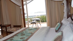 A bedroom with a large bed, a chair, a table, and a balcony with a view. - Ryan's Bay Hotel (Mwanza)
