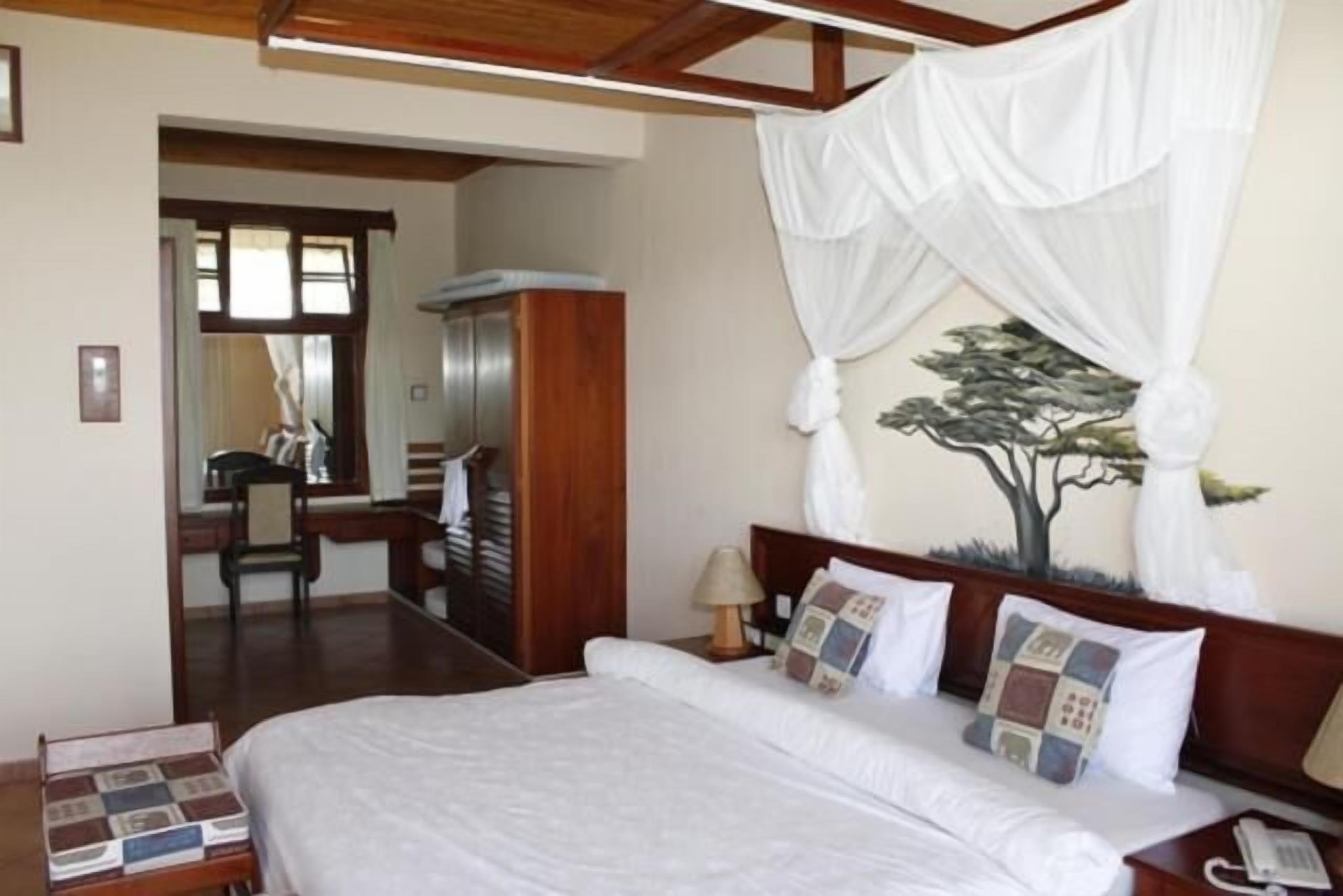 A hotel room with a bed, a desk, a chair, a wardrobe, and a nightstand.