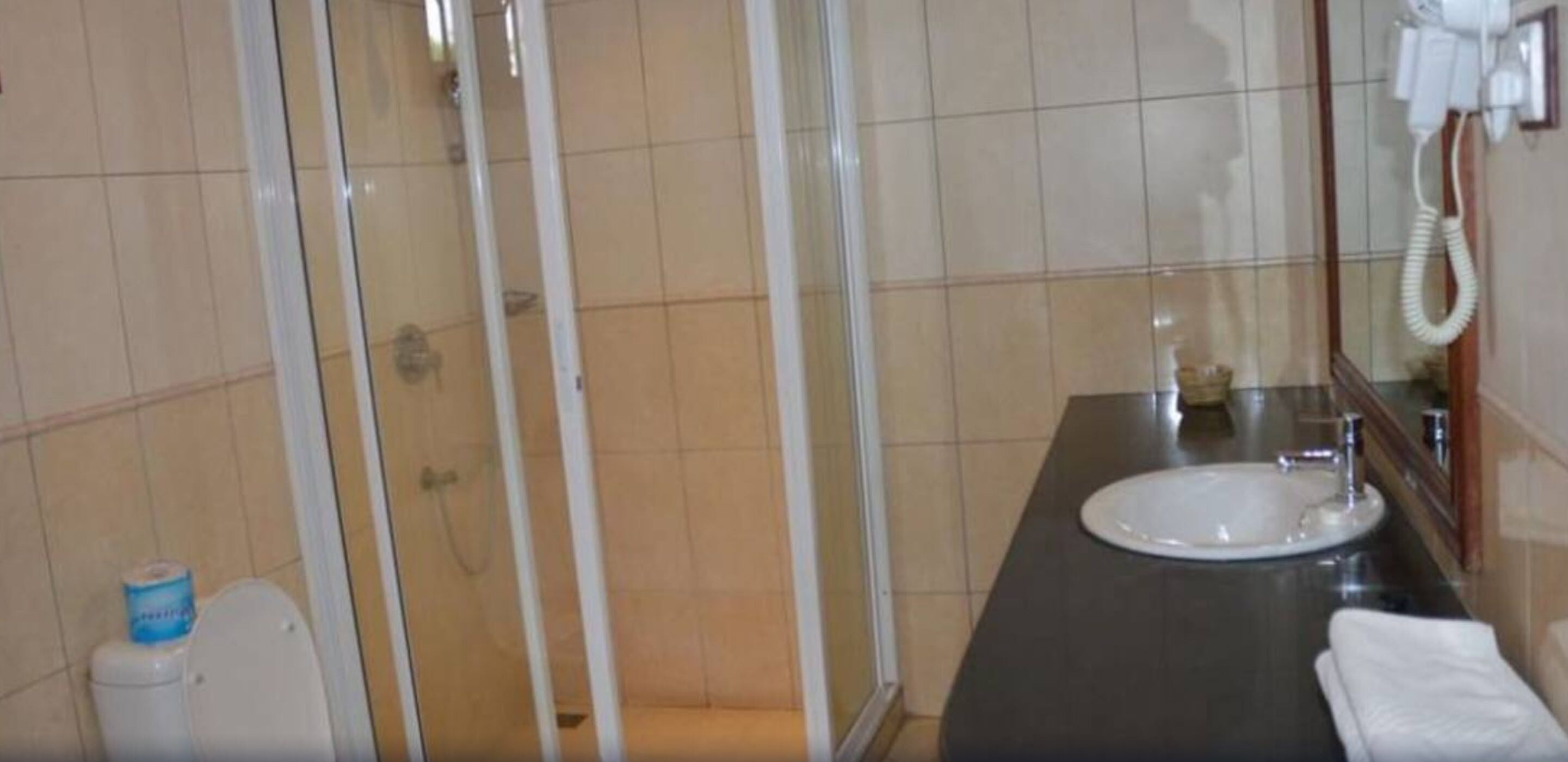 Un baño con ducha, inodoro, lavamanos y secador de pelo sujeto a la pared.