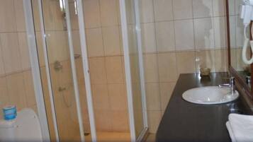 Un baño con ducha, inodoro, lavamanos y secador de pelo sujeto a la pared.