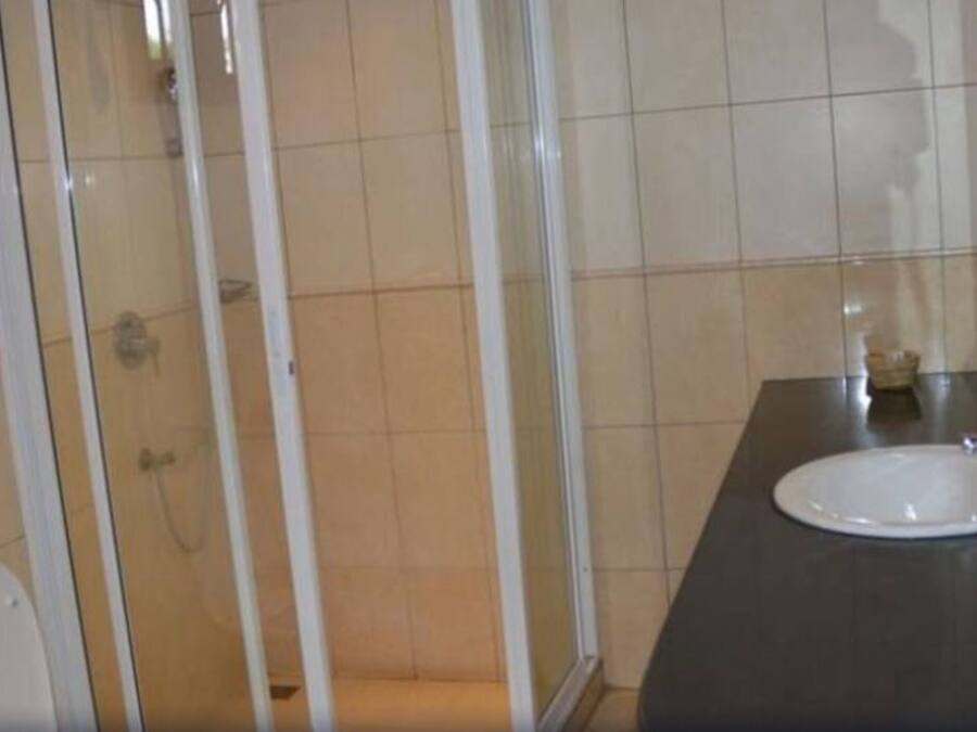 Un baño con ducha, inodoro, lavamanos y secador de pelo sujeto a la pared.