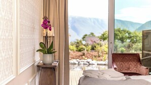 A bedroom with a bed, a potted orchid, and a view of a mountainous landscape through a glass door. - Walaker Hotel (Luster)