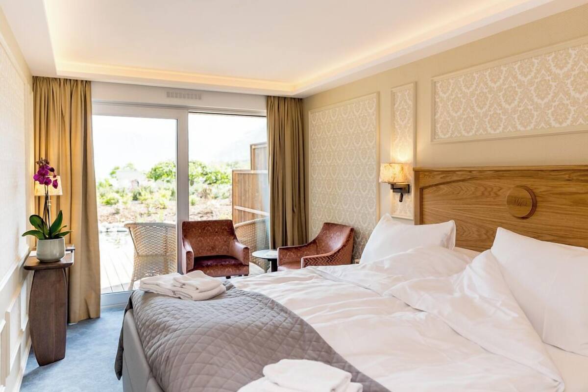 A hotel room with a bed, a chair, a small table, and a view of the outdoors.