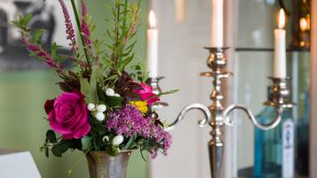 A table with a metal vase containing flowers and a candle holder with two lit candles.