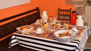 A breakfast table with various breakfast items and beverages, set against a stone wall and wooden furniture. - Picabreiz (Cast)
