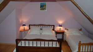 A bedroom with a sloped ceiling, a bed with a wooden headboard, two bedside tables with lamps, and a small framed picture on the wall. - Picabreiz (Cast)