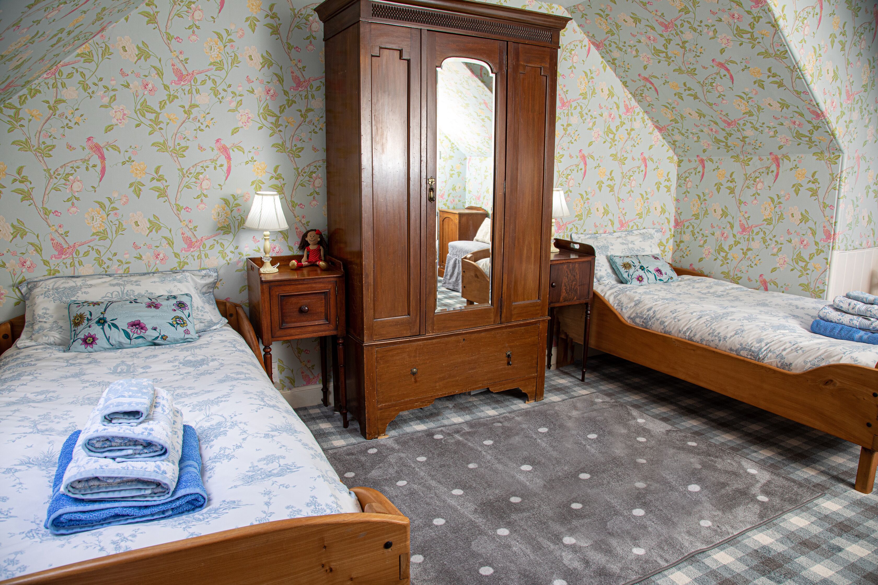 Une chambre à coucher avec deux lits en bois, une armoire et un papier peint à motifs floraux.