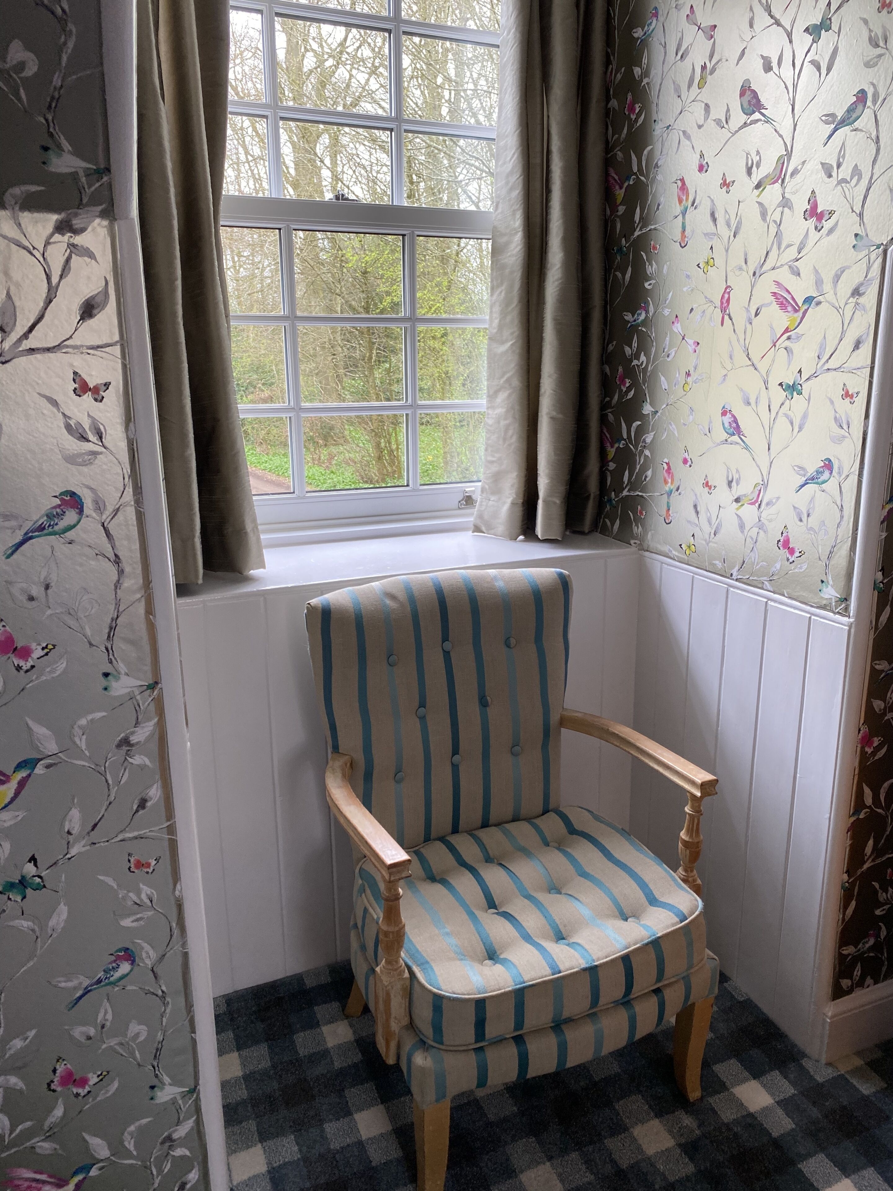 A corner room with a window, a striped armchair, and floral wallpaper.
