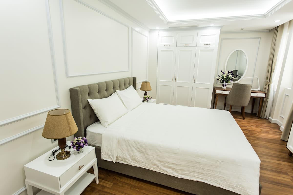 A neatly arranged bedroom with a bed, bedside tables, a desk, and a chair.