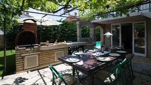 An outdoor patio with a brick fireplace, a dining table set for four, and a covered seating area. - Villa Bramasole ,big pool , View 200m sea, Kamenjak Park, EV charging available (Premantura)