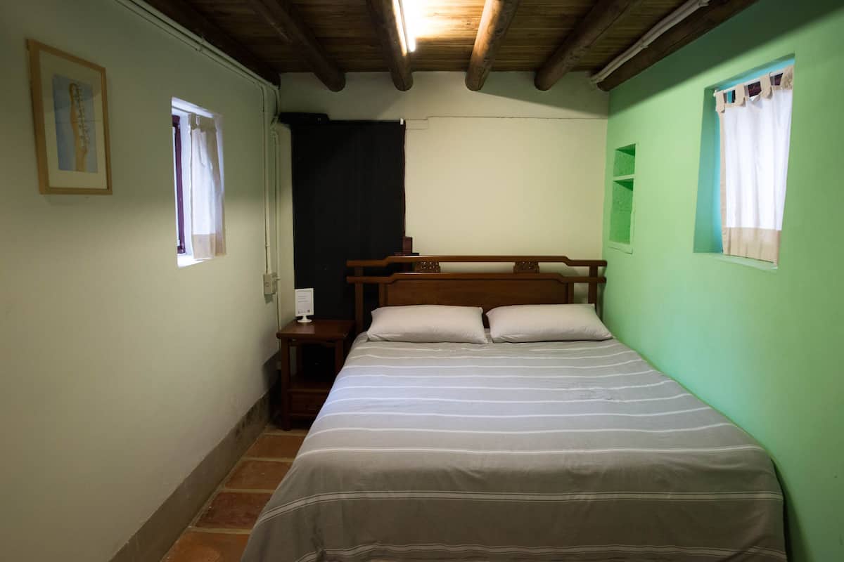 A room with a bed, a nightstand, a window, and a wooden ceiling.