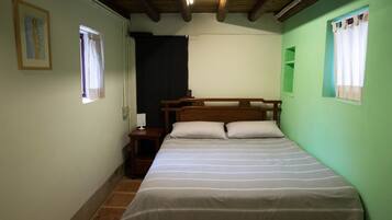 A room with a bed, a nightstand, a window, and a wooden ceiling.