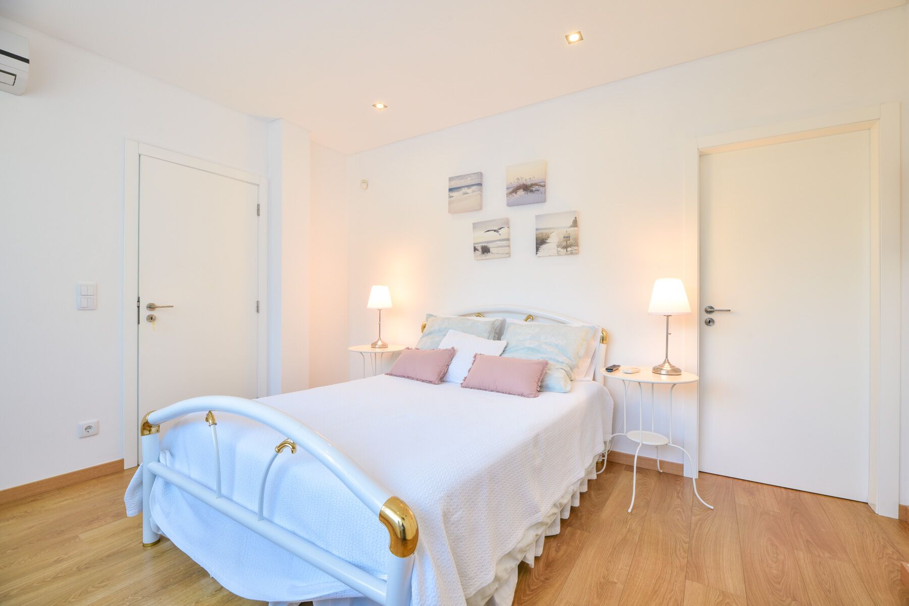Een slaapkamer met een wit bed, twee nachtkastjes met lampen, een witte deur en een muur met drie ingelijste foto's.