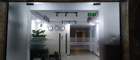 An indoor entrance with a glass door, a red carpet, potted plants, and clocks indicating different time zones.