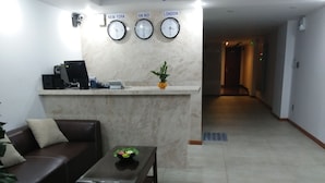 A reception area with a reception desk, a brown leather sofa, a wooden coffee table, and a potted plant. - R&G Suite (Ho Chi Minh City)