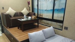 A compact room with a bed, a sofa, and a coffee table. There is a painting of a beach scene on the wall. - R&G Suite (Ho Chi Minh City)