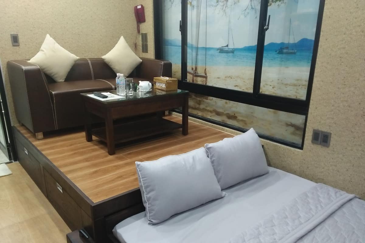 A compact room with a bed, a sofa, and a coffee table. There is a painting of a beach scene on the wall.