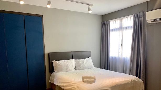 Una cama bien hecha con ropa blanca y una toalla blanca, cabecera oscura y suelo de madera.