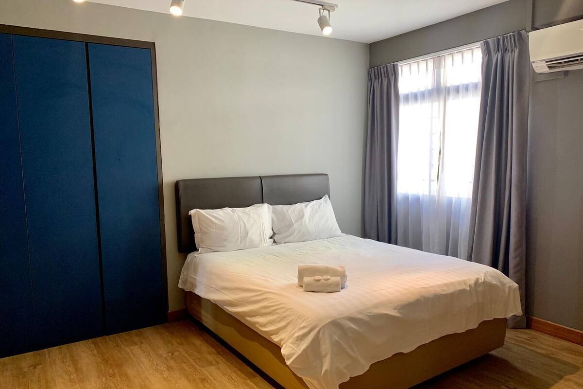 Un lit bien fait, avec du linge de lit blanc et une serviette blanche, une tête de lit sombre et un plancher en bois.