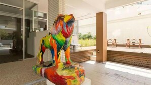 Una escultura colorida de león en un área exterior moderna, con entrada por puerta de cristal y un patio con mesas de madera.