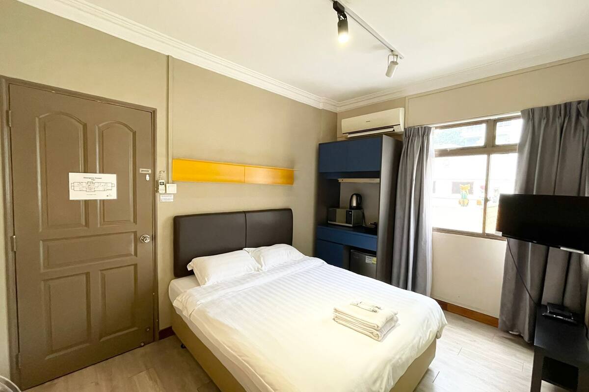 Une chambre d’hôtel équipée d’un lit, d’une télévision, d’un bureau, d’une armoire et d’une fenêtre avec des rideaux.