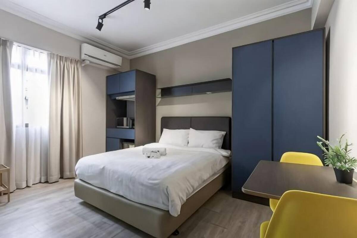 Une chambre d’hôtel moderne équipée d’un lit, d’un bureau, d’une chaise, d’une plante et d’étagères intégrées.