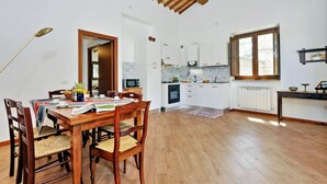 Un comedor con una mesa y sillas de madera, una cocina con armarios blancos y un ventanal con vistas.