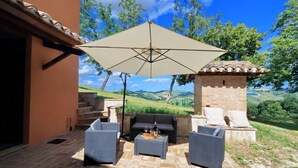 Un patio al aire libre con mobiliario de mimbre, una sombrilla grande y un muro de piedra.