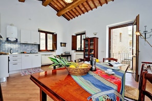 A modern kitchen with white cabinets, a wooden dining table, and a view of the street through large windows.
