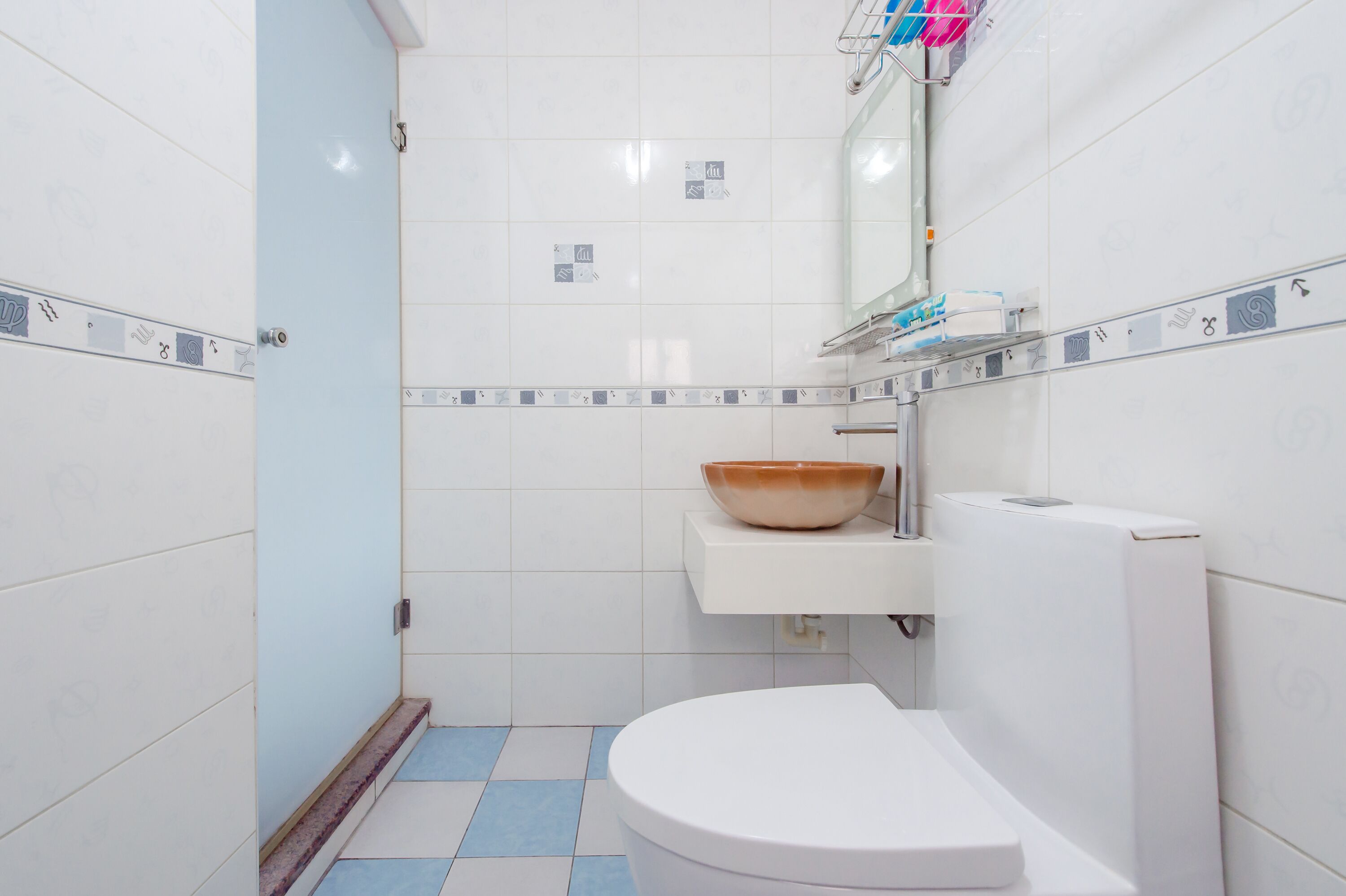 A bathroom with a white toilet, a sink with a brown bowl, and a mirror above the sink.