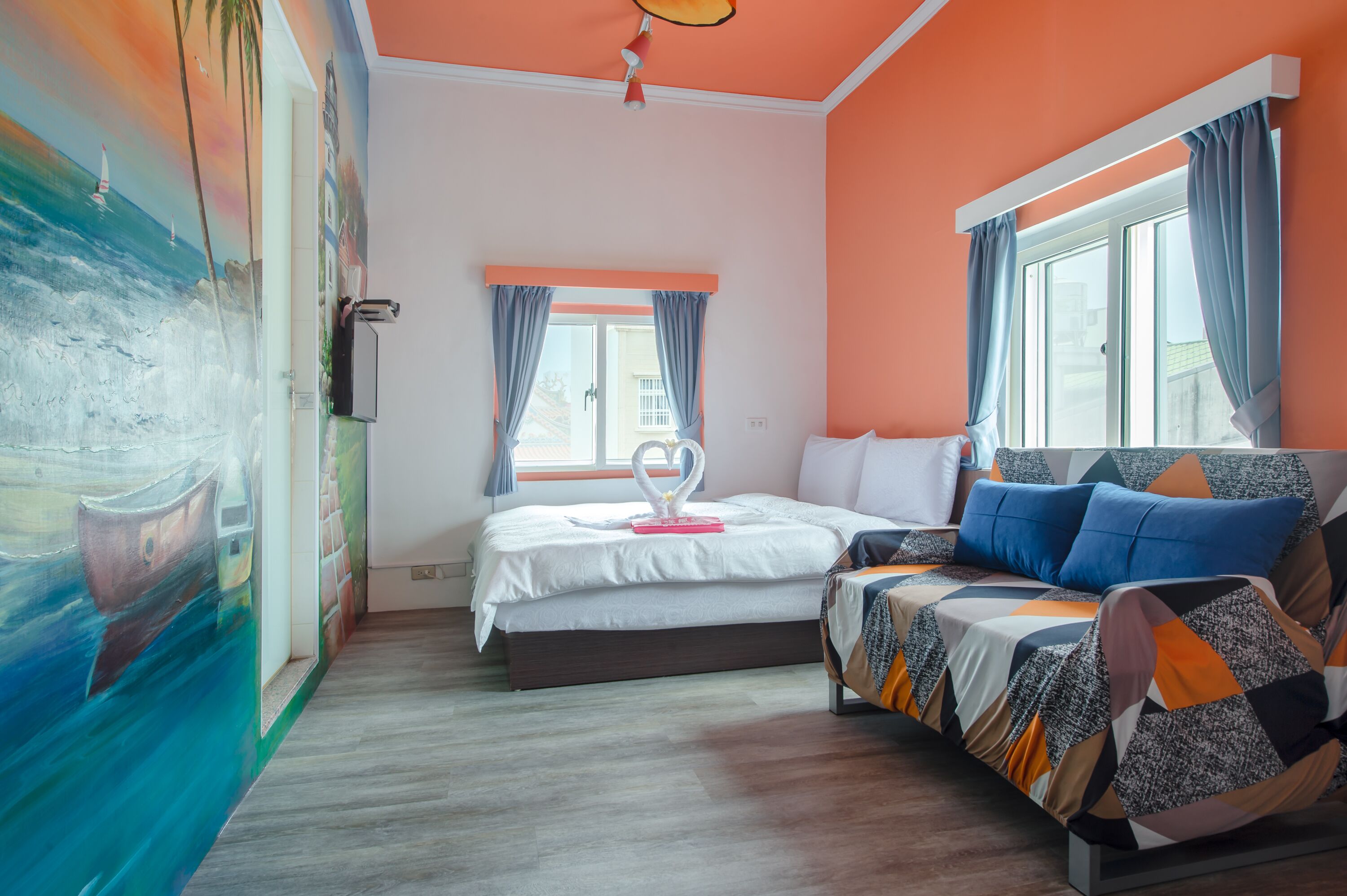 A bedroom with a bed, a sofa, a window with curtains, a painting on the wall, and a ceiling light.