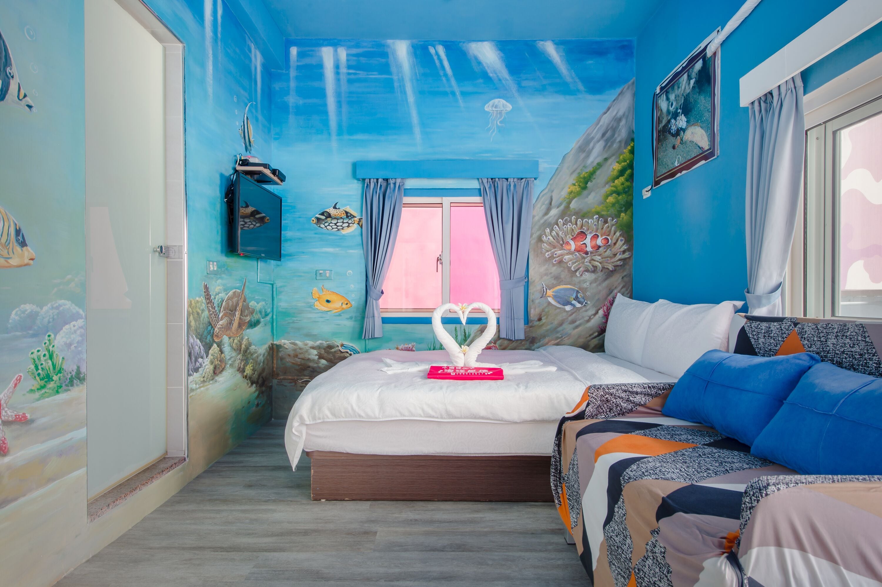 Una habitación con una cama, un ventanal con cortinas y un mural en la pared que representa una escena submarina.