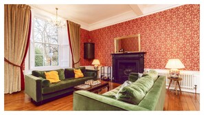 A living room with green sofas, a fireplace, and a patterned wallpaper.