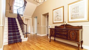 A spacious hallway with a wooden floor, a staircase with a plaid carpet, and a wooden cabinet with drawers. - A Georgian Masterpiece Steps from Stirling  (Stirling)