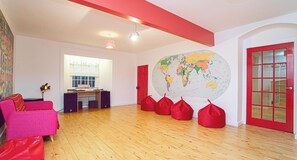 A spacious room with a wooden floor, a red couch, a world map on the wall, and a red door.